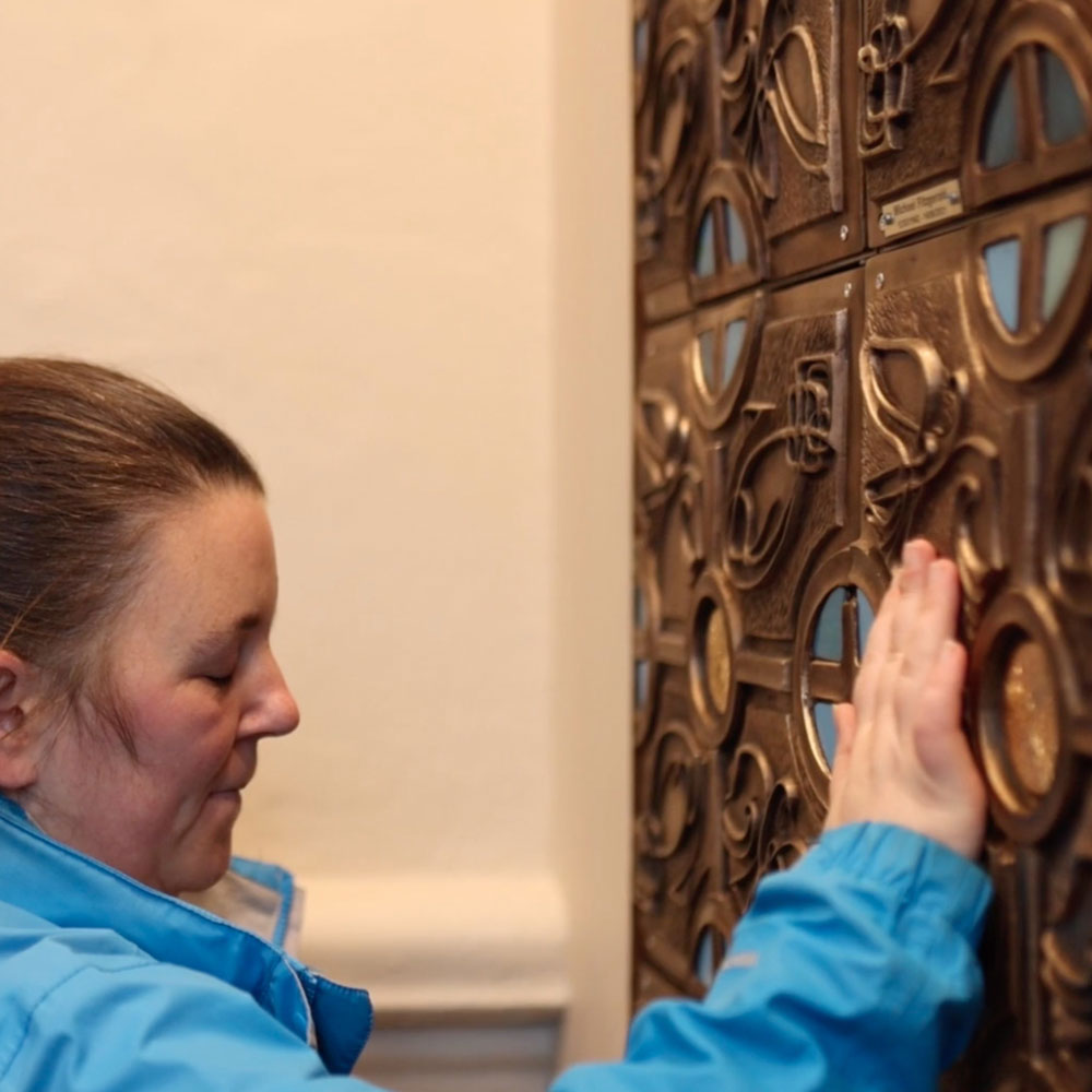 A member of staff fitting a memorial plaque to a columbarium